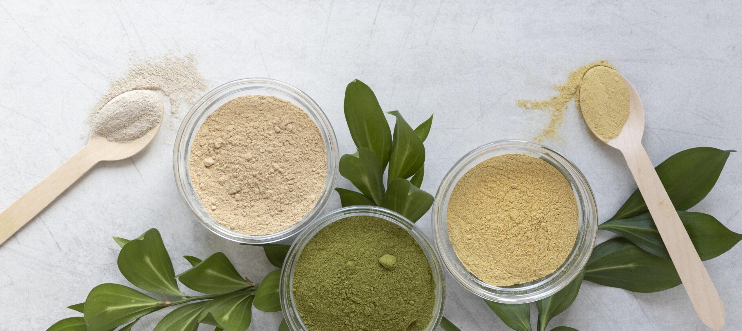 vegan proteine poeder, 3 verschillende poeders met lepeltjes, groen, geel en beige van kleur op een achtergrond van blaadjes